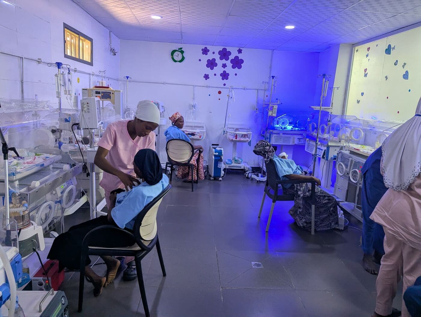 The incubator bay under its lamps, a nurse attending a mother at the edge of the room