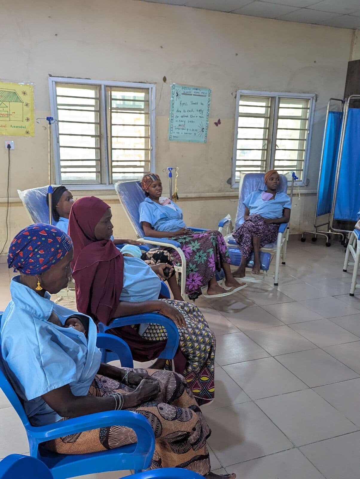 Mothers in Kangaroo Care chairs along the ward, their newborns held against them
