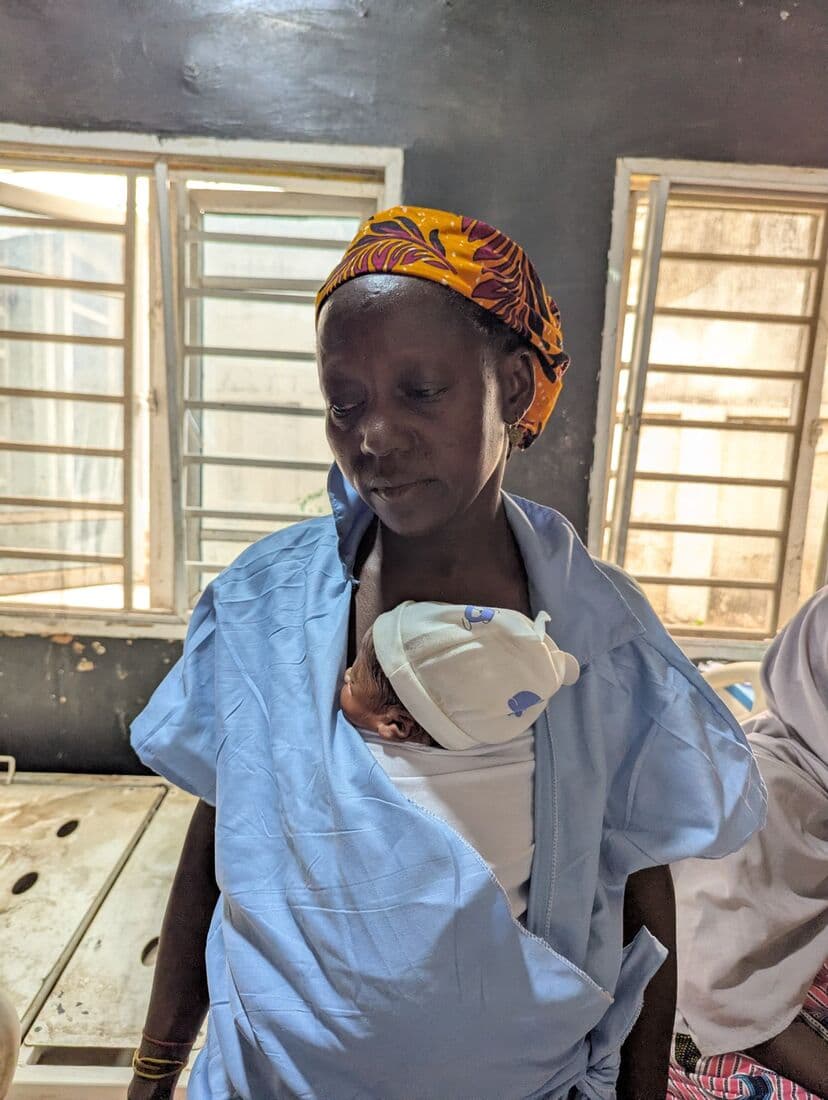 A mother at the window of the ward looking down at her newborn against her chest