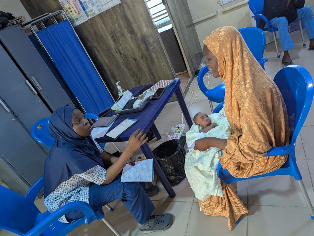 A nurse entering a mother's Kangaroo Care record at the ward desk, her newborn in her arms