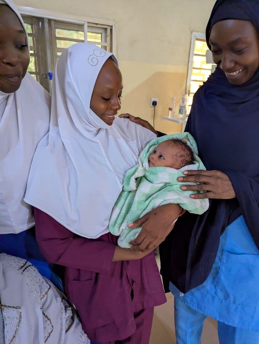 Two nurses in Kano holding a newborn wrapped in a green blanket