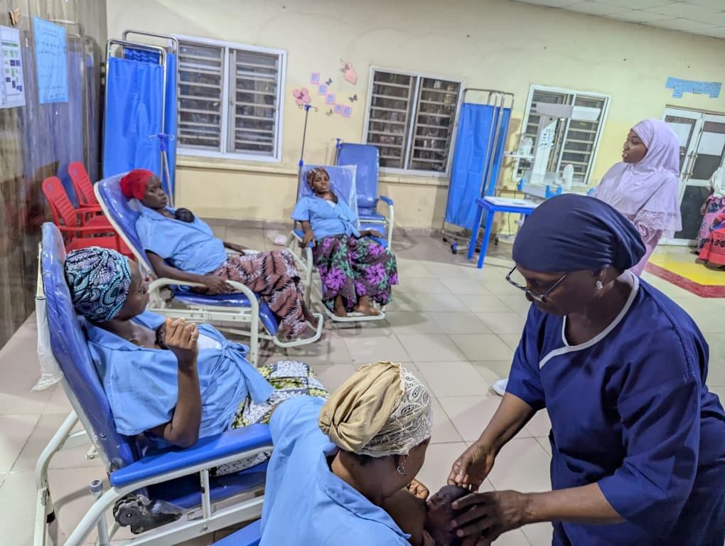 A nurse kneeling beside a mother in a Kangaroo Care chair, taking her hands